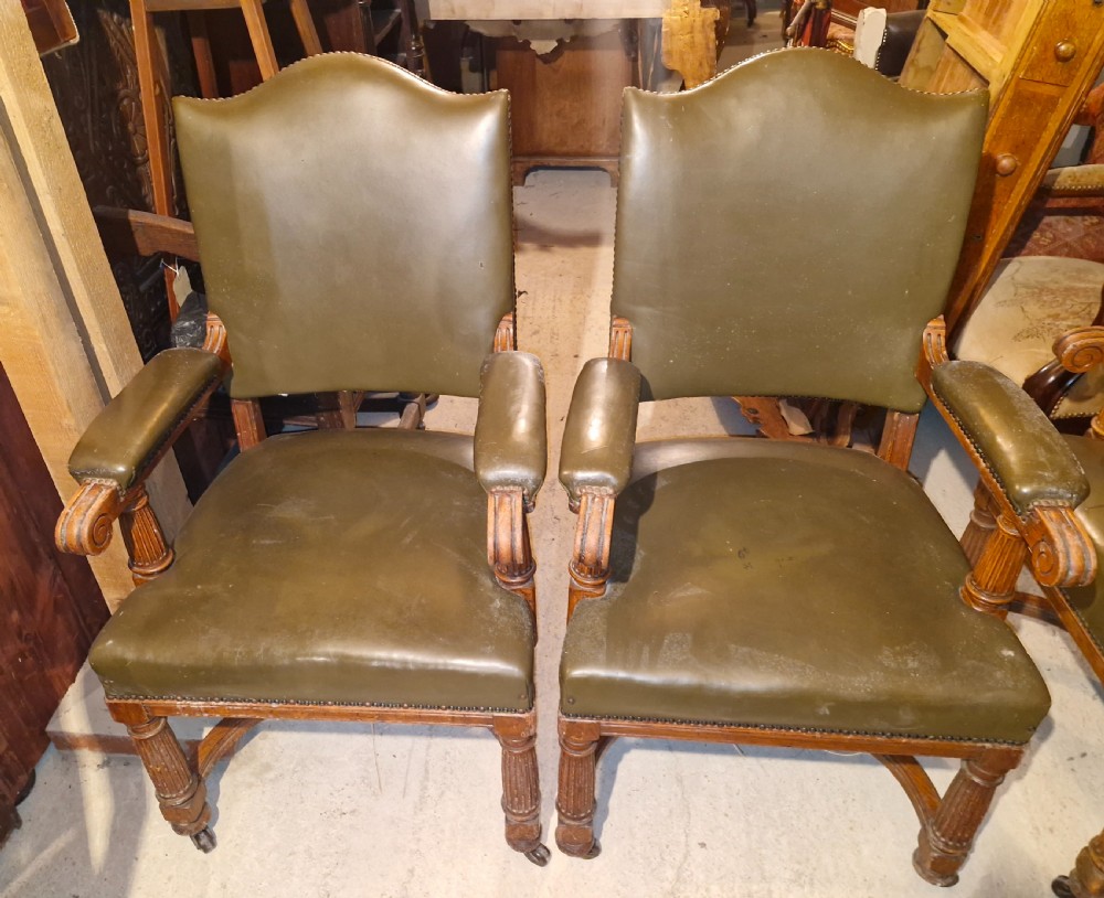 A pair of late Victorian oak desk armchairs upholstered in olive green leather with brass stud detailing and fluted front legs on castors.