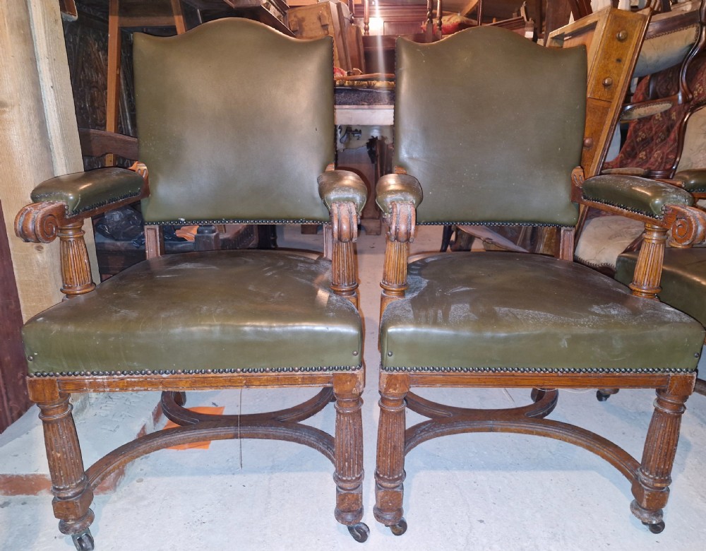 A pair of late Victorian oak desk armchairs upholstered in olive green leather with brass stud detailing and fluted front legs on castors. View V