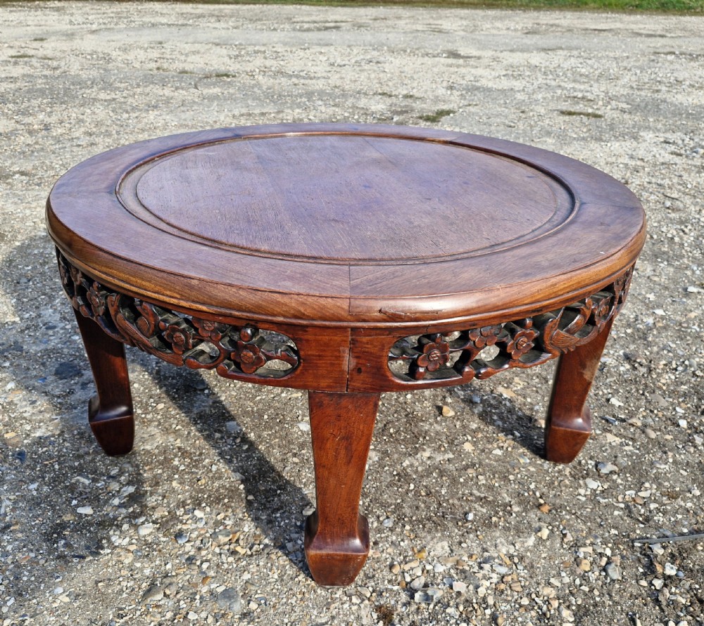 A low circular Chinese hardwood coffee table featuring an intricately carved openwork floral apron and curved legs.