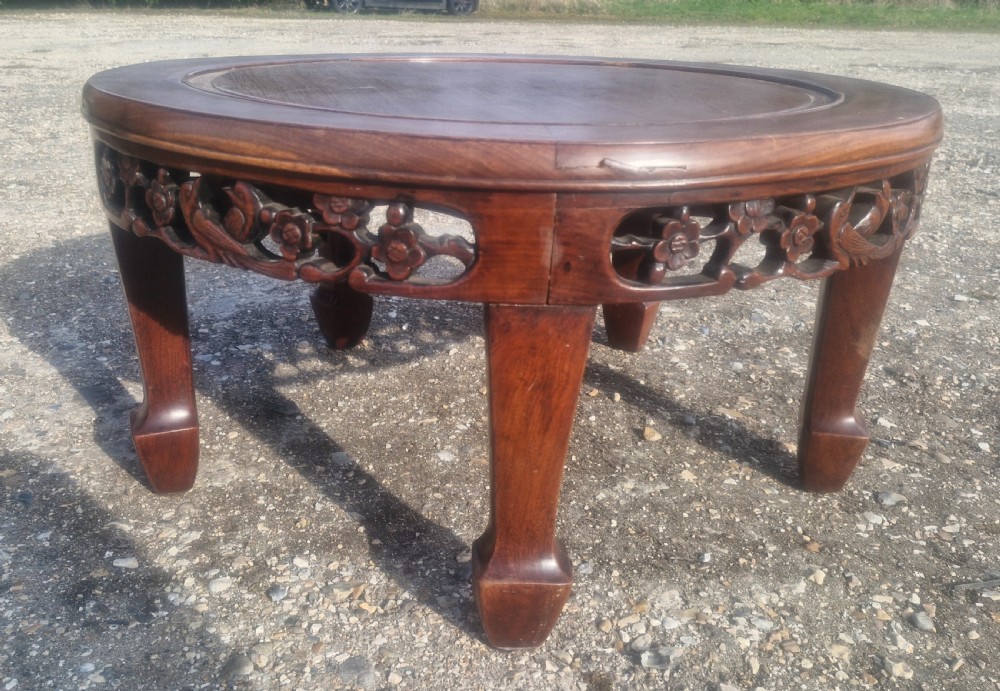 A low circular Chinese hardwood coffee table featuring an intricately carved openwork floral apron and curved legs. View II