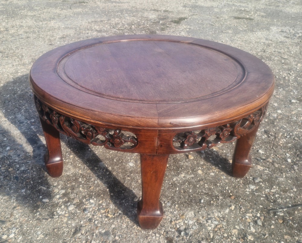 A low circular Chinese hardwood coffee table featuring an intricately carved openwork floral apron and curved legs. View V