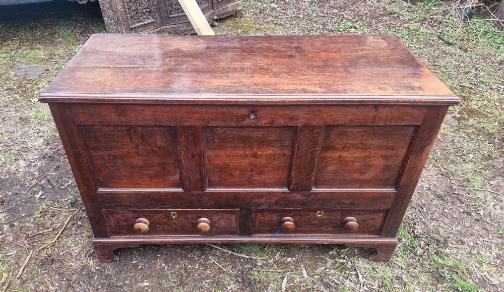 A late Georgian dark oak mule chest featuring a hinged top lid, three front panels, two lower drawers with turned wooden knobs, and bracket feet.