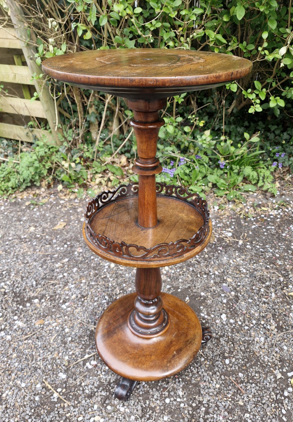 An early Victorian rosewood decanter table featuring a circular top, a central turned stem with a fretwork-gallery lower tier, and a circular base with scroll feet.