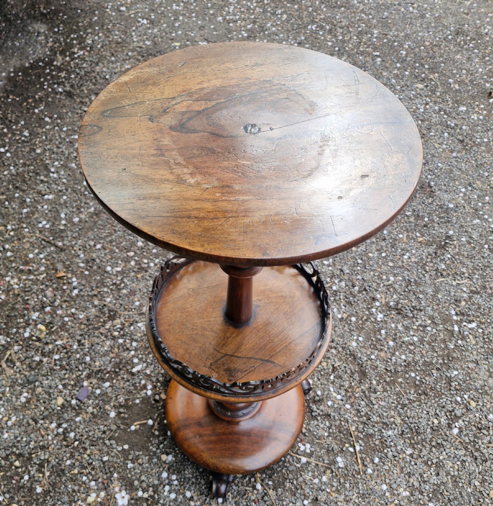 An early Victorian rosewood decanter table featuring a circular top, a central turned stem with a fretwork-gallery lower tier, and a circular base with scroll feet. View V