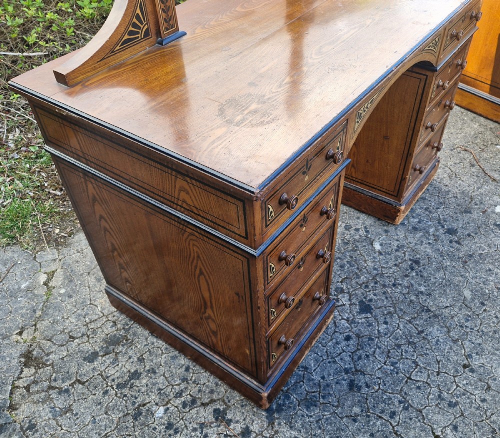 A late Victorian warm brown wood pedestal dressing table featuring ebonised stencilled accents, turned mirror supports, and nine drawers flanking a central kneehole. View II