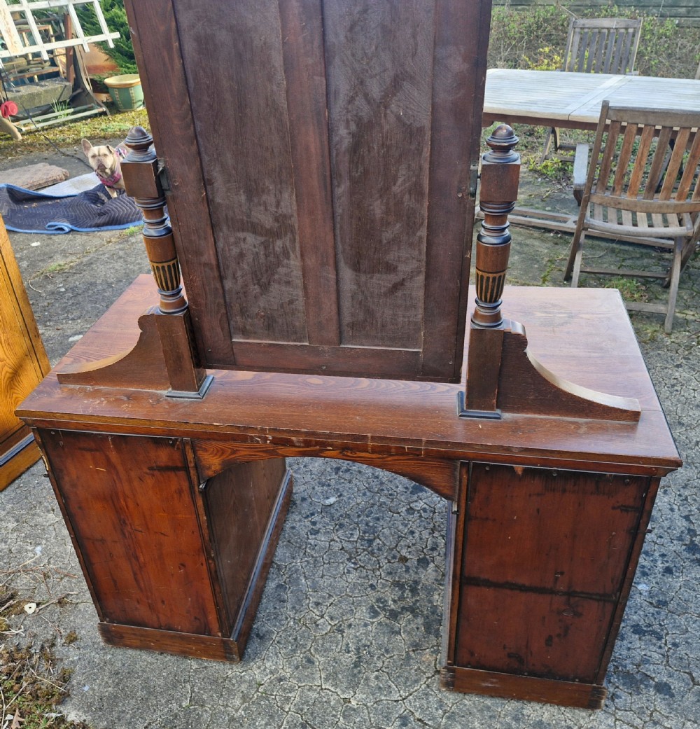 A late Victorian warm brown wood pedestal dressing table featuring ebonised stencilled accents, turned mirror supports, and nine drawers flanking a central kneehole. View III