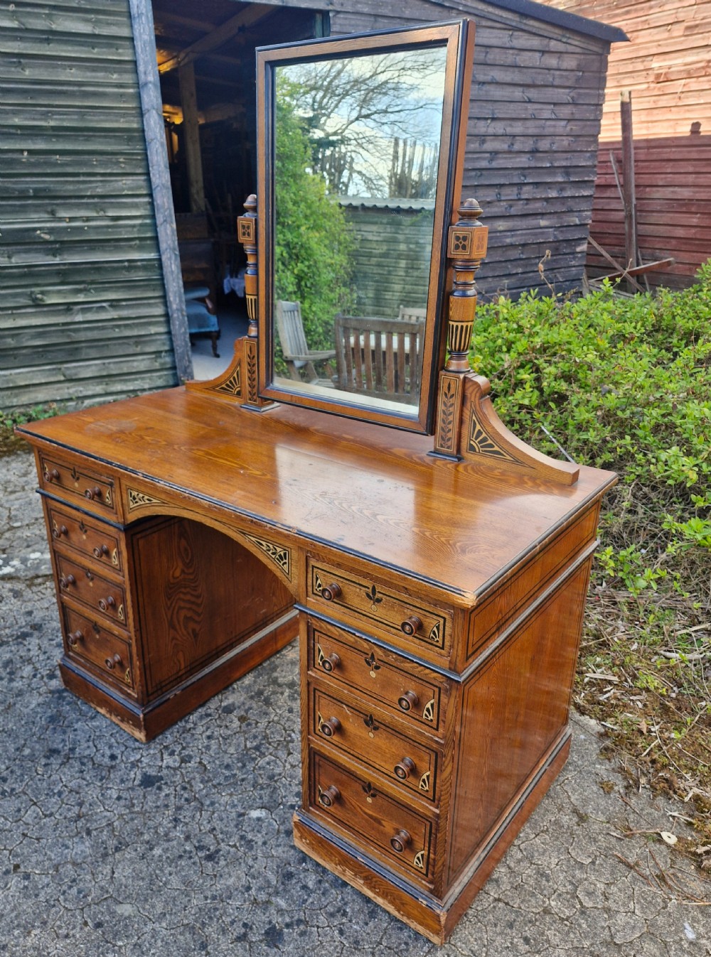 A late Victorian warm brown wood pedestal dressing table featuring ebonised stencilled accents, turned mirror supports, and nine drawers flanking a central kneehole. View V