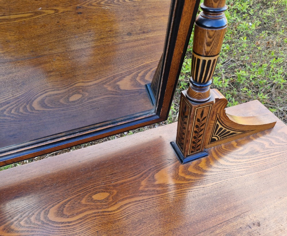 A late Victorian warm brown wood pedestal dressing table featuring ebonised stencilled accents, turned mirror supports, and nine drawers flanking a central kneehole. View VI