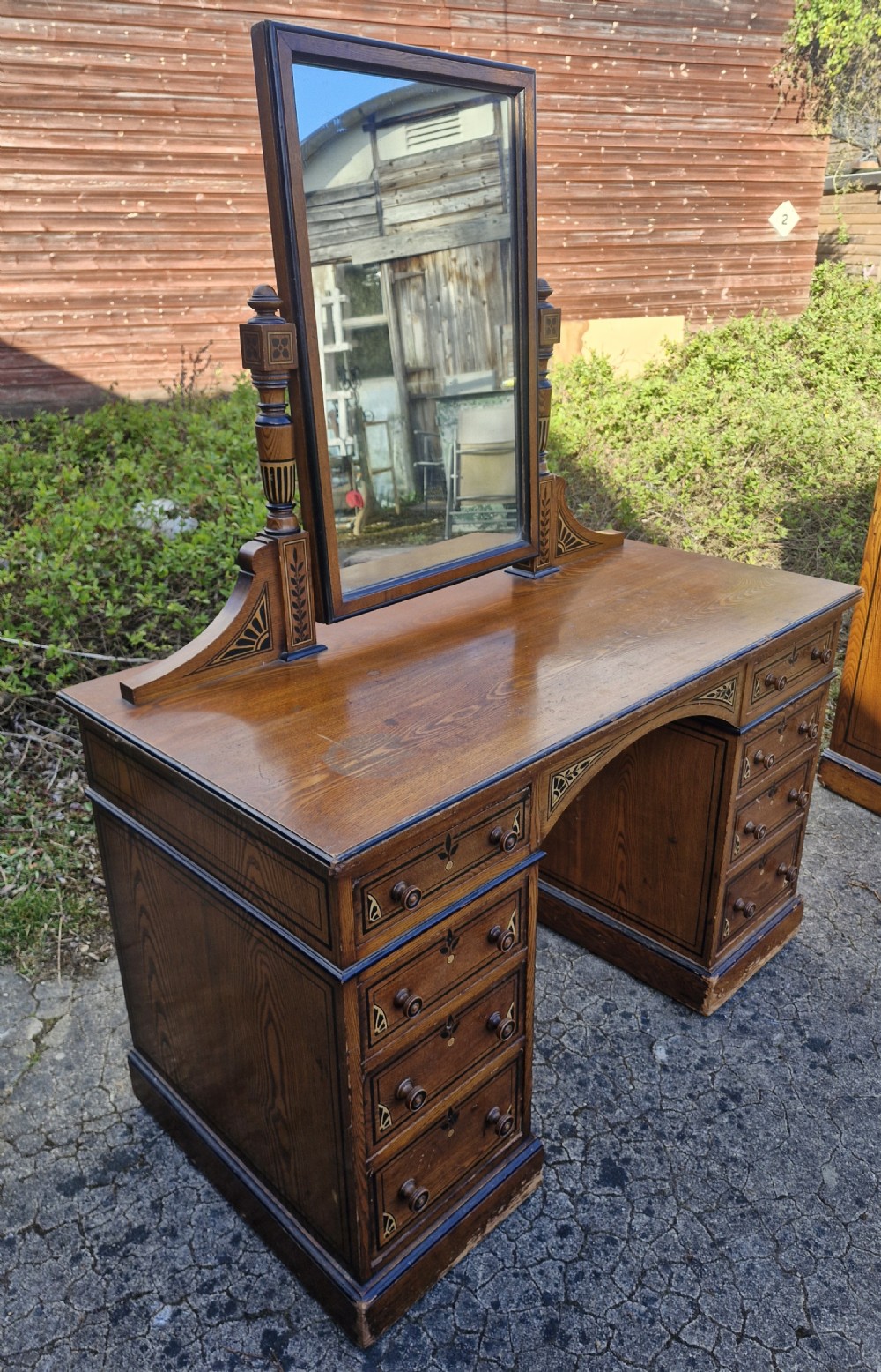 A late Victorian warm brown wood pedestal dressing table featuring ebonised stencilled accents, turned mirror supports, and nine drawers flanking a central kneehole. View VII