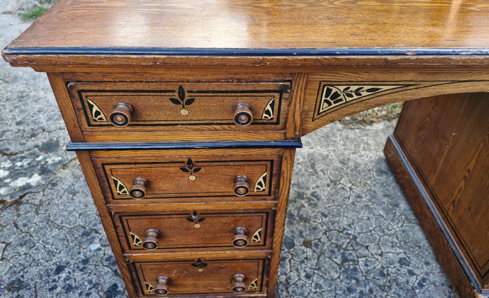A late Victorian warm brown wood pedestal dressing table featuring ebonised stencilled accents, turned mirror supports, and nine drawers flanking a central kneehole. View VIII