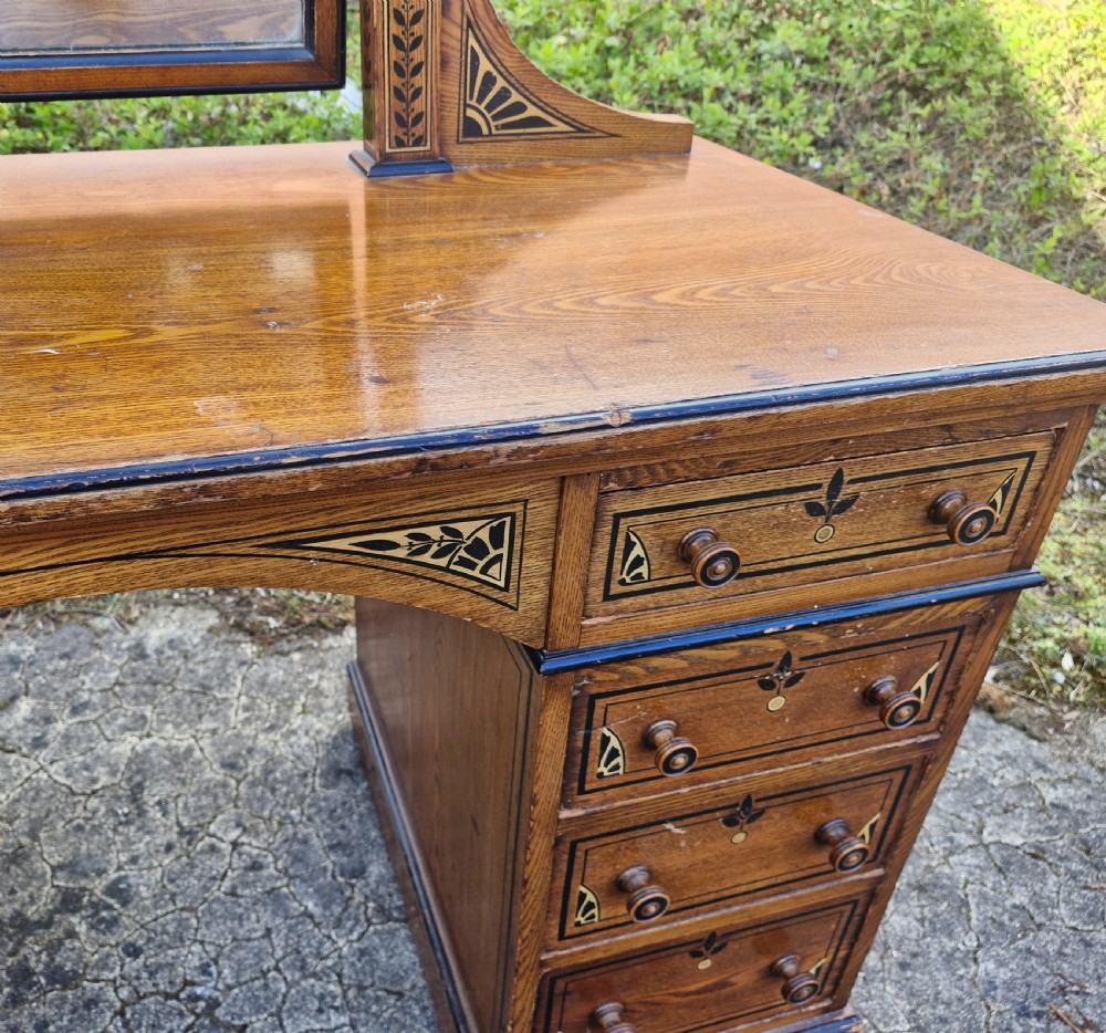 A late Victorian warm brown wood pedestal dressing table featuring ebonised stencilled accents, turned mirror supports, and nine drawers flanking a central kneehole. View IX