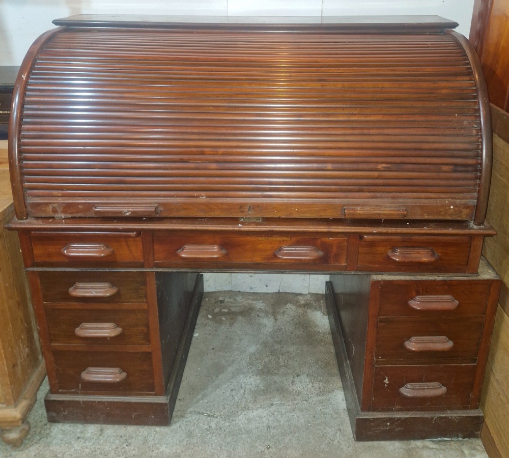 A large mahogany pedestal desk featuring a flexible slatted tambour roll-top hood above multiple drawers with carved wood pulls.