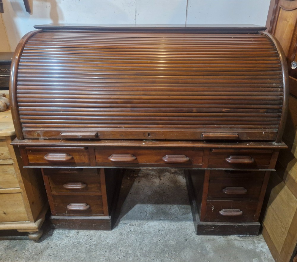 A large mahogany pedestal desk featuring a flexible slatted tambour roll-top hood above multiple drawers with carved wood pulls. View II