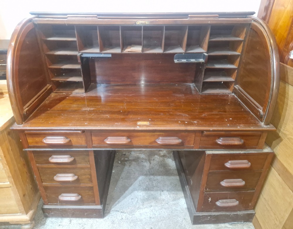A large mahogany pedestal desk featuring a flexible slatted tambour roll-top hood above multiple drawers with carved wood pulls. View III