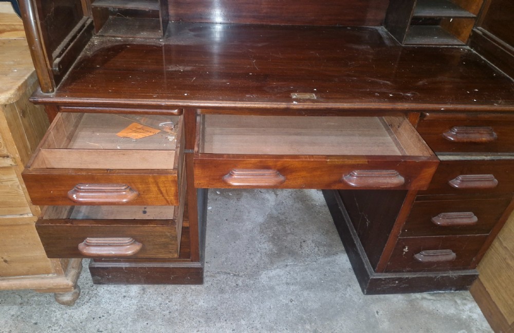 A large mahogany pedestal desk featuring a flexible slatted tambour roll-top hood above multiple drawers with carved wood pulls. View V