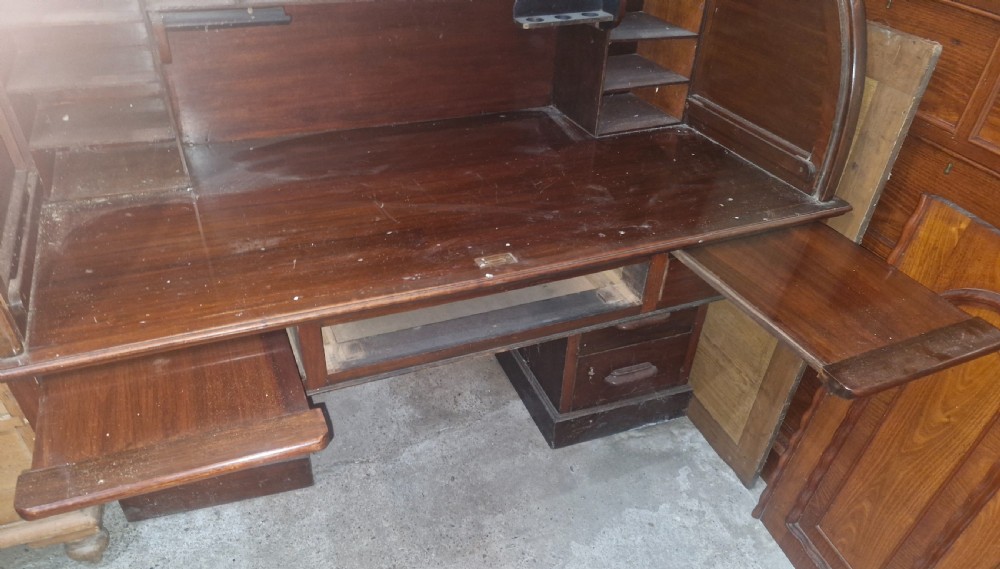 A large mahogany pedestal desk featuring a flexible slatted tambour roll-top hood above multiple drawers with carved wood pulls. View VI