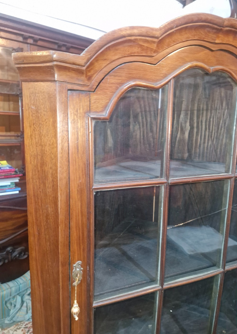 A tall early 20th-century walnut corner display cabinet featuring two sections, arched glazed doors, and a shaped pediment top. View II