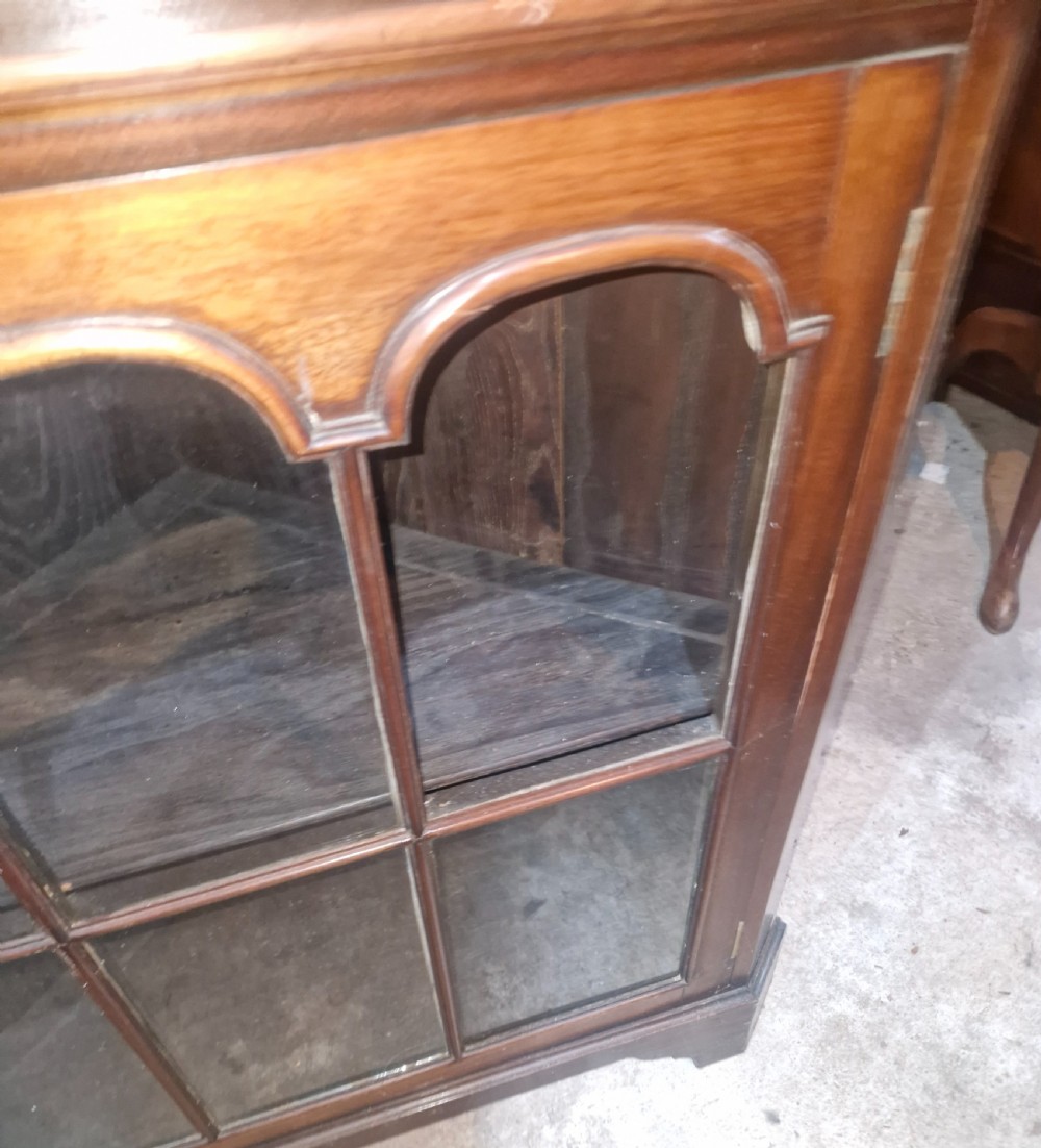 A tall early 20th-century walnut corner display cabinet featuring two sections, arched glazed doors, and a shaped pediment top. View III
