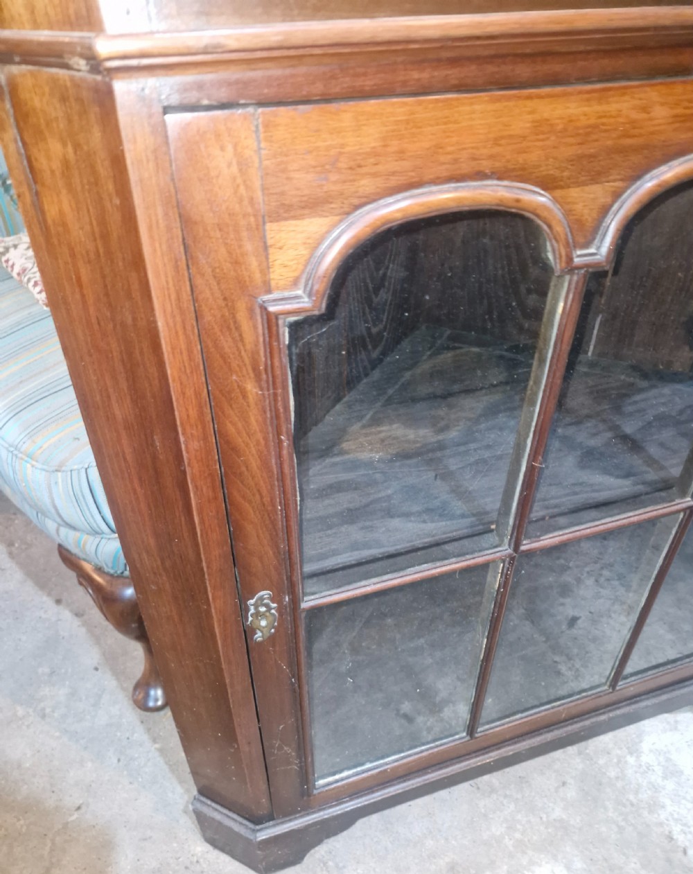 A tall early 20th-century walnut corner display cabinet featuring two sections, arched glazed doors, and a shaped pediment top. View IV