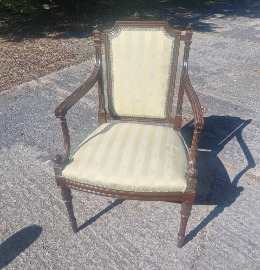 An Edwardian open armchair featuring a dark mahogany frame with fluted front legs, shaped arms, corner finials, and pale yellow striped upholstery.