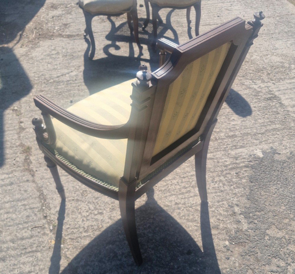 An Edwardian open armchair featuring a dark mahogany frame with fluted front legs, shaped arms, corner finials, and pale yellow striped upholstery. View II