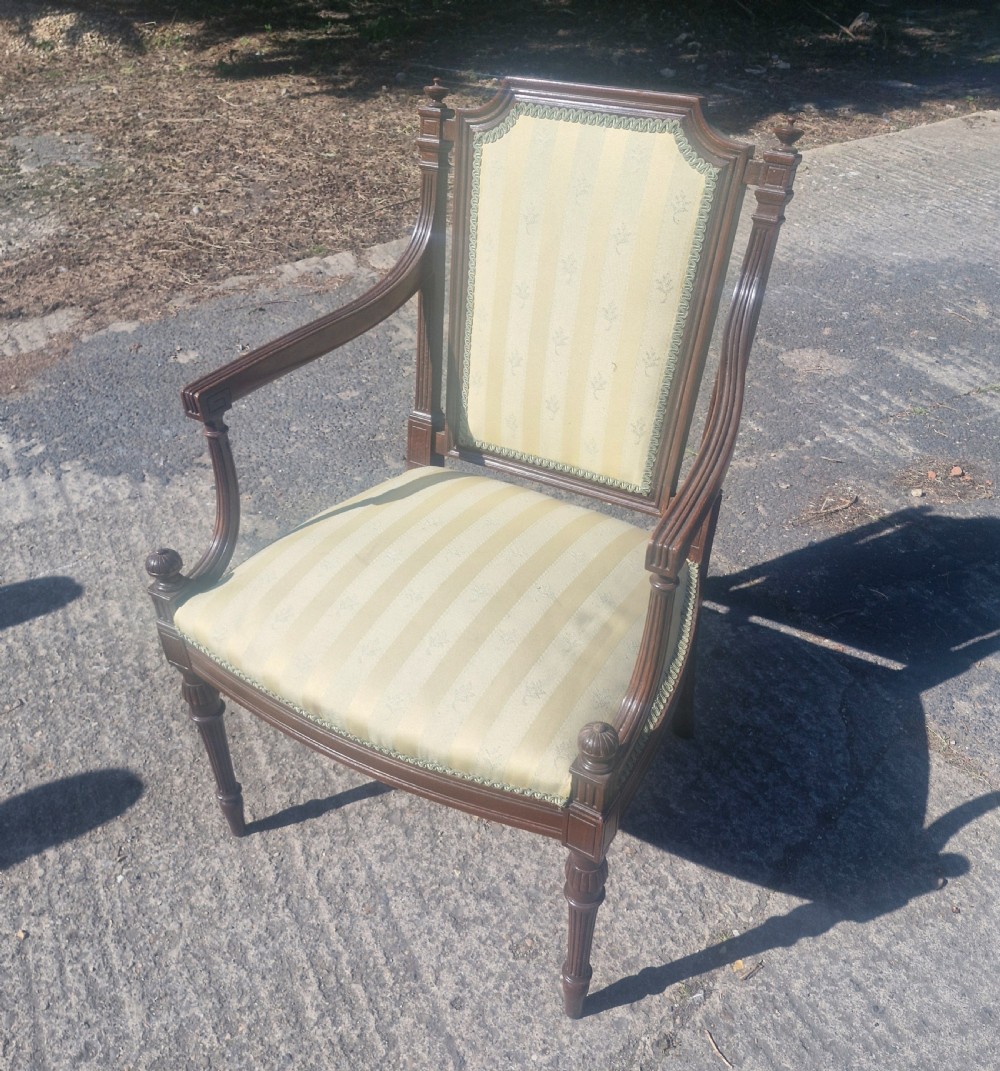 An Edwardian open armchair featuring a dark mahogany frame with fluted front legs, shaped arms, corner finials, and pale yellow striped upholstery. View IV
