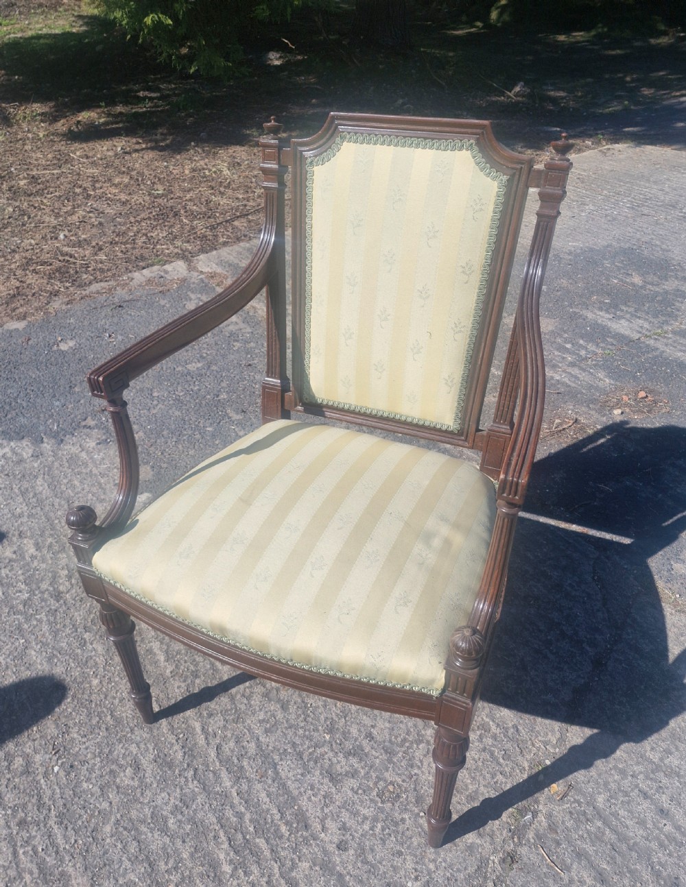 An Edwardian open armchair featuring a dark mahogany frame with fluted front legs, shaped arms, corner finials, and pale yellow striped upholstery. View V