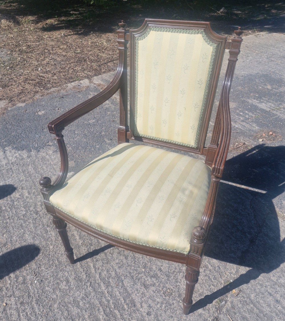 An Edwardian open armchair featuring a dark mahogany frame with fluted front legs, shaped arms, corner finials, and pale yellow striped upholstery. View VI