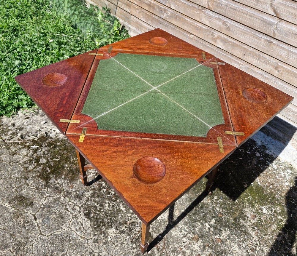 An Edwardian square mahogany envelope games table featuring foliate marquetry inlay, a single drawer with brass drop handles, a lower undertier, and tapered legs. View II
