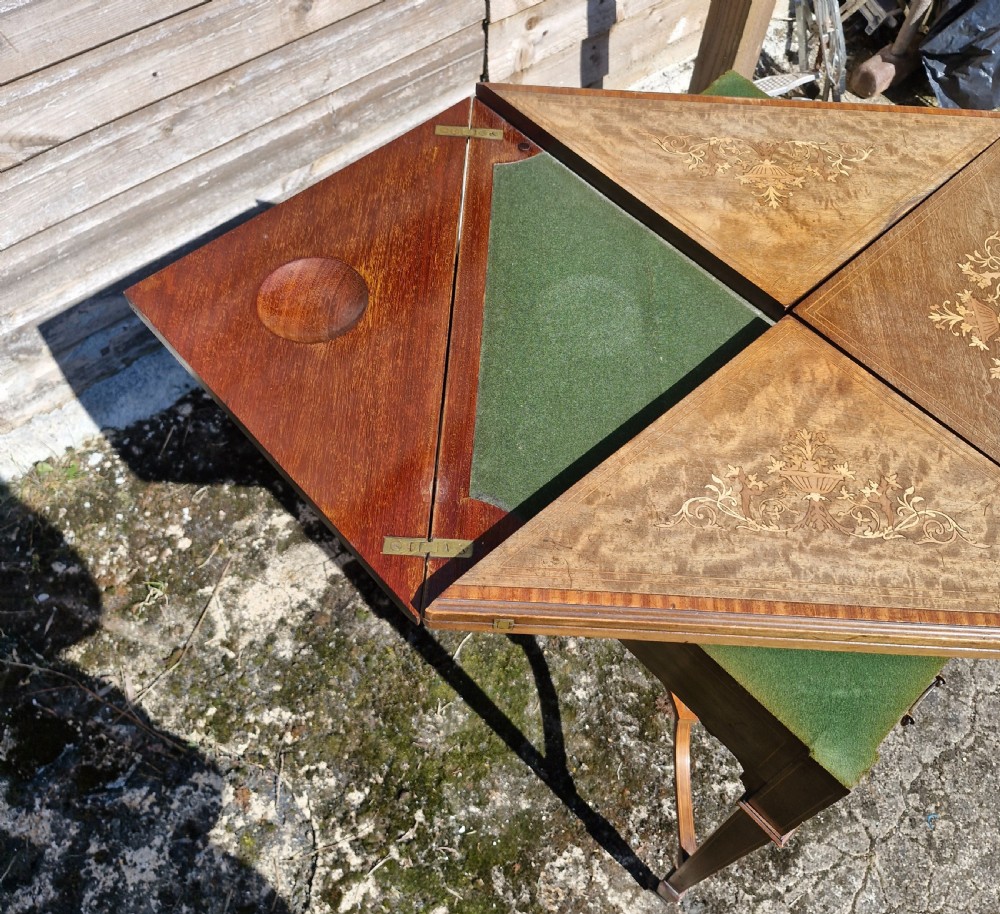 An Edwardian square mahogany envelope games table featuring foliate marquetry inlay, a single drawer with brass drop handles, a lower undertier, and tapered legs. View IV