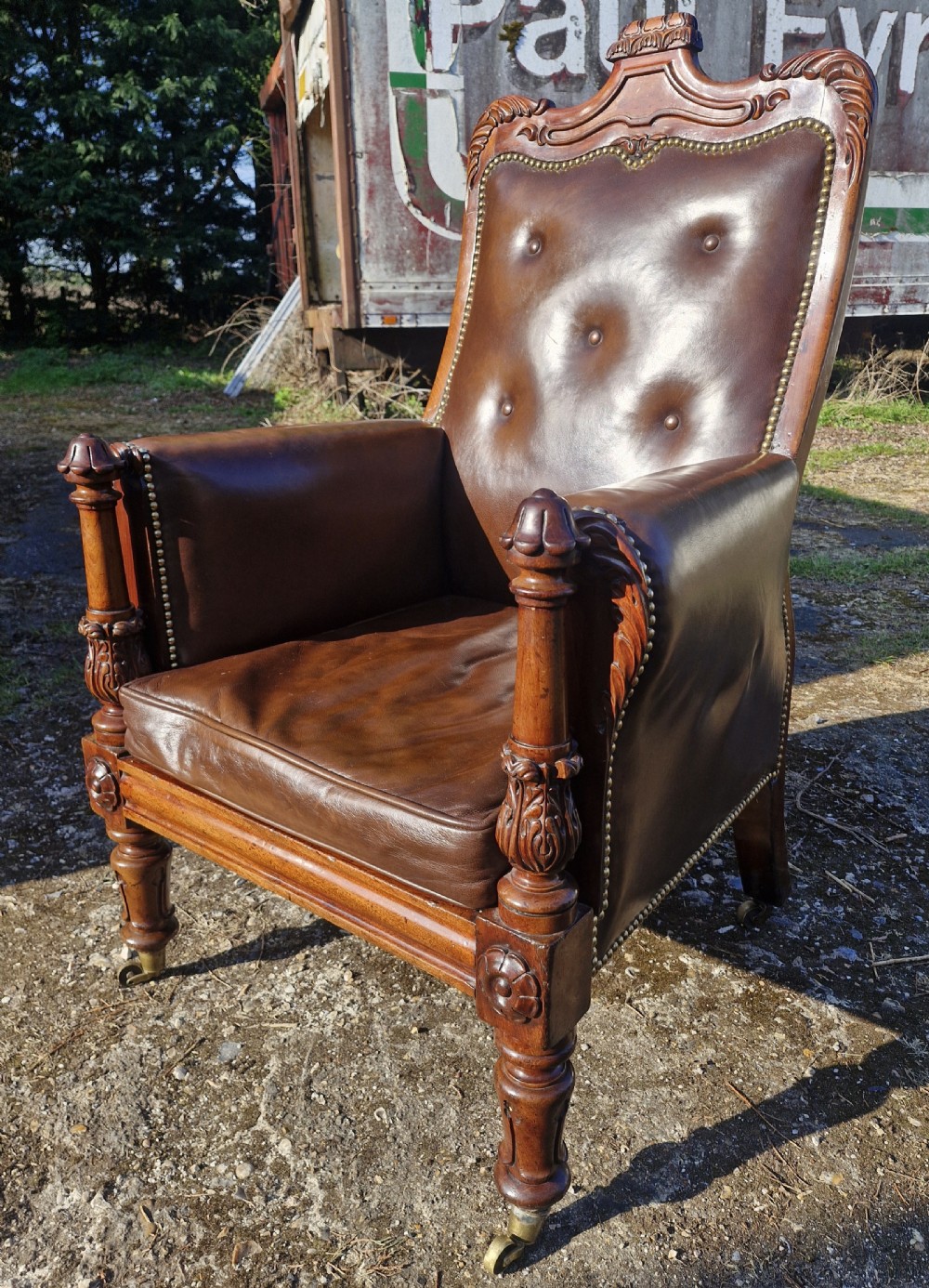 A Regency style mahogany library armchair upholstered in button-tufted brown leather with carved detailing and brass castors. View II