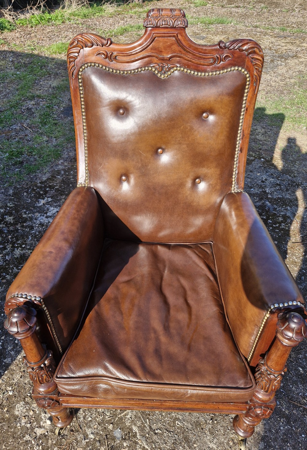 A Regency style mahogany library armchair upholstered in button-tufted brown leather with carved detailing and brass castors. View III