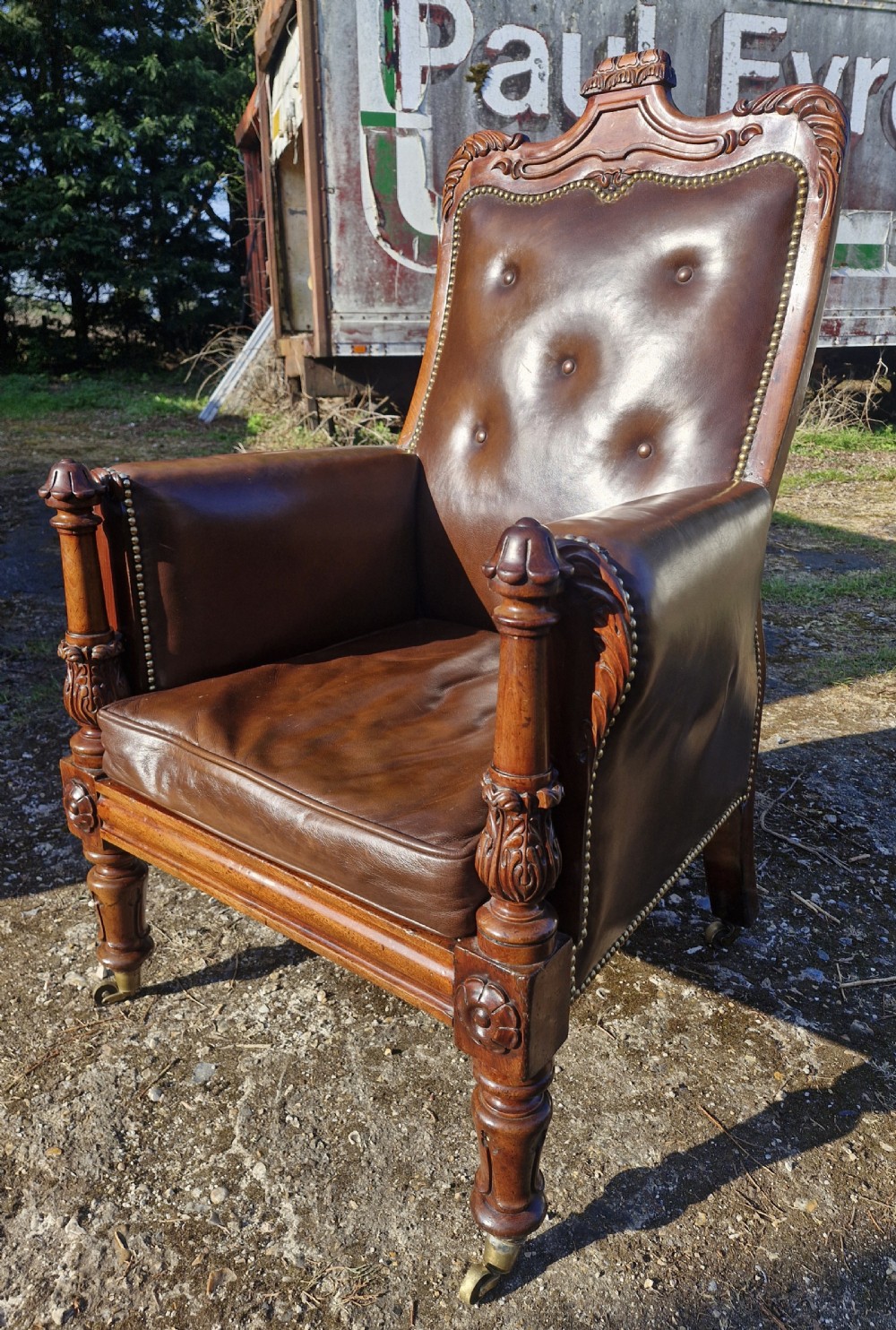 A Regency style mahogany library armchair upholstered in button-tufted brown leather with carved detailing and brass castors. View VIII