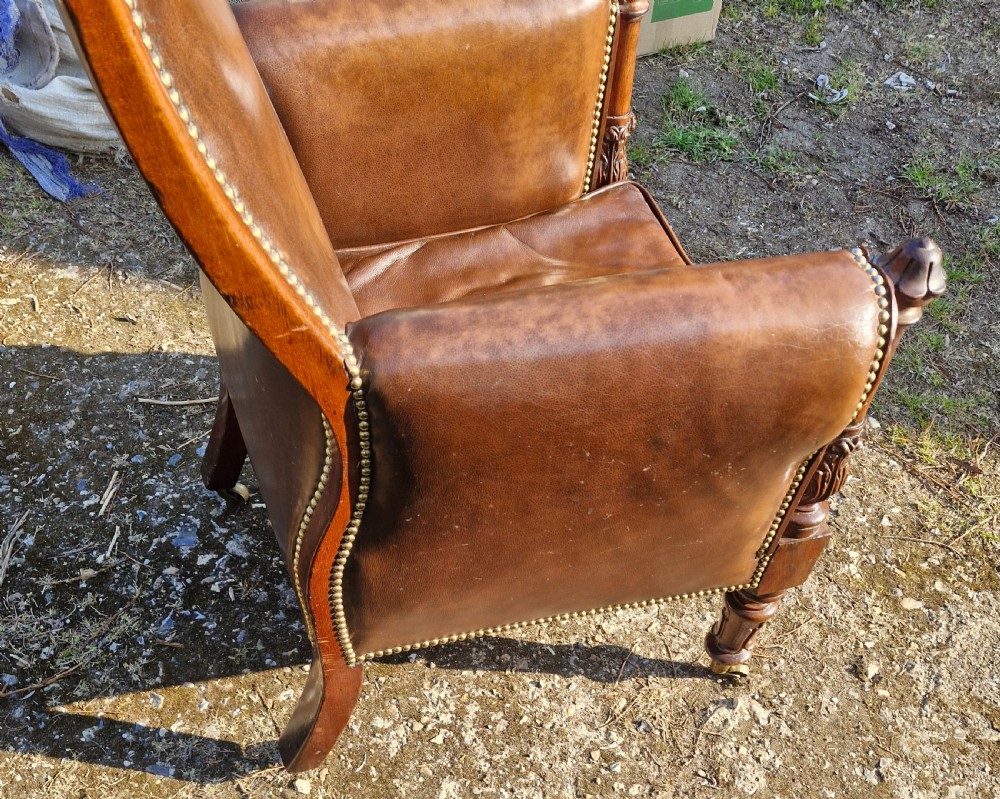 A Regency style mahogany library armchair upholstered in button-tufted brown leather with carved detailing and brass castors. View IX