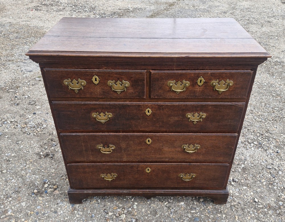 A dark oak Georgian chest of drawers featuring a two-over-three drawer arrangement, decorative brass handles, keyholes, and bracket feet.