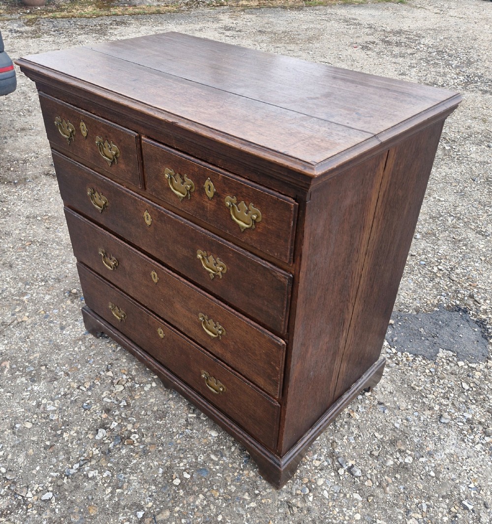 A dark oak Georgian chest of drawers featuring a two-over-three drawer arrangement, decorative brass handles, keyholes, and bracket feet. View IV