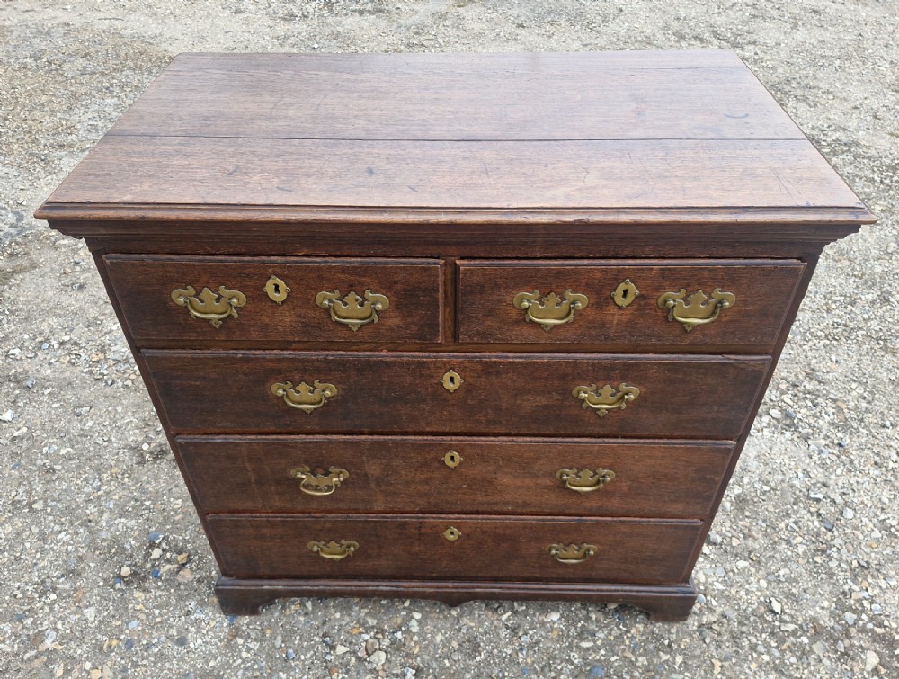 A dark oak Georgian chest of drawers featuring a two-over-three drawer arrangement, decorative brass handles, keyholes, and bracket feet. View V