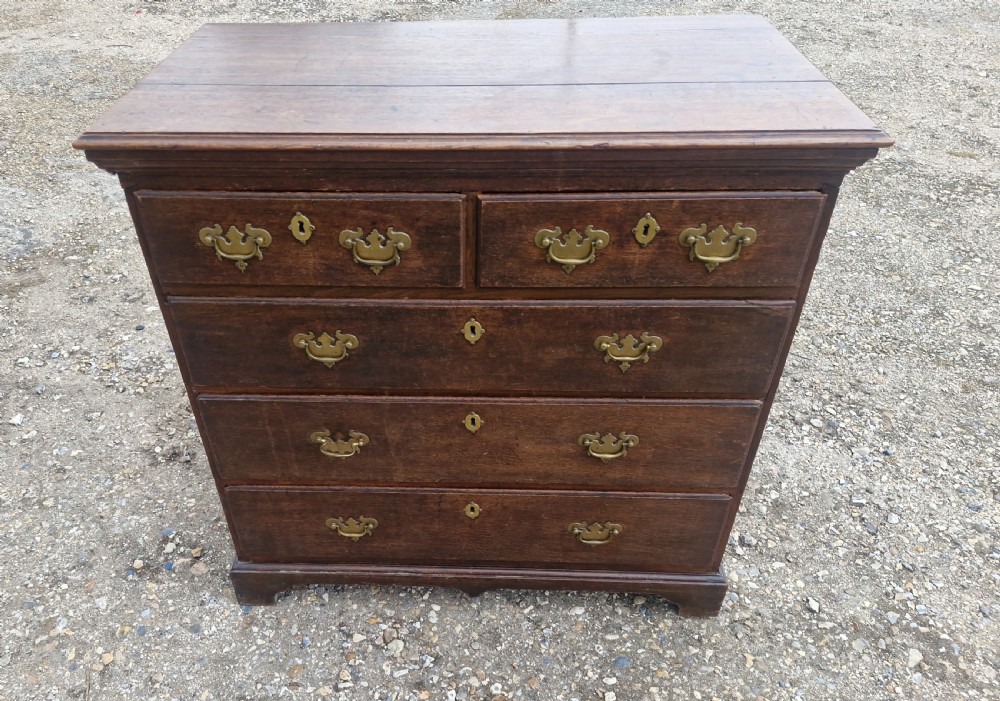 A dark oak Georgian chest of drawers featuring a two-over-three drawer arrangement, decorative brass handles, keyholes, and bracket feet. View VI