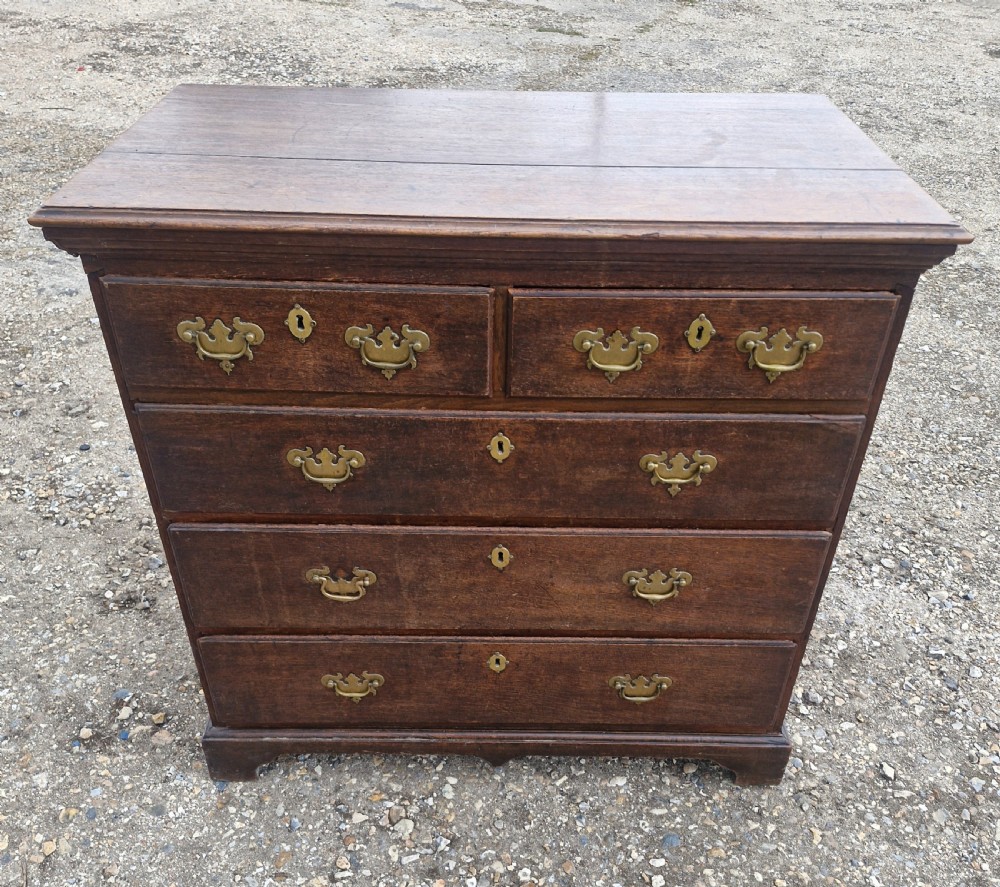 A dark oak Georgian chest of drawers featuring a two-over-three drawer arrangement, decorative brass handles, keyholes, and bracket feet. View VII