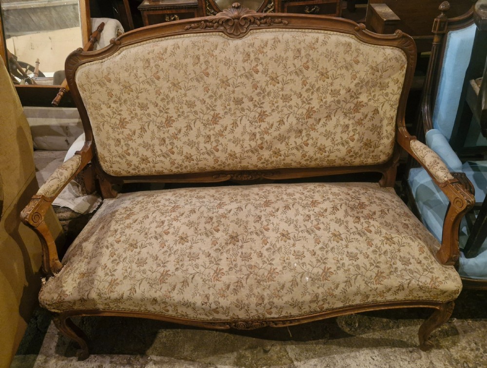 A small French Louis XV style two-seater sofa with a carved walnut frame, cabriole legs, floral top cresting, and patterned beige textile upholstery. View X