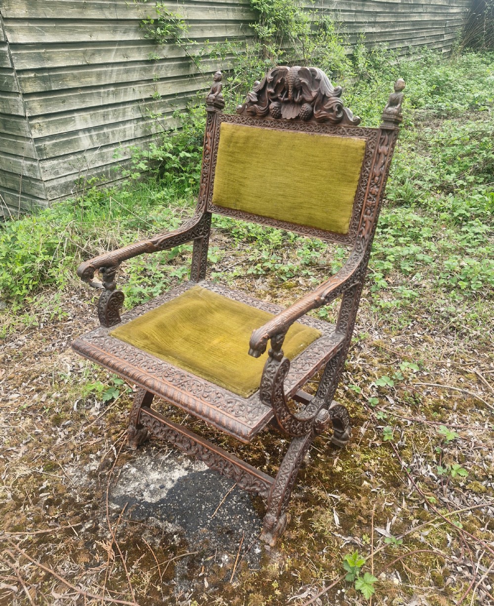 A detailed carved dark wood Anglo-Indian armchair featuring an elephant motif cresting, figural finials, and olive green velvet seat and back upholstery.