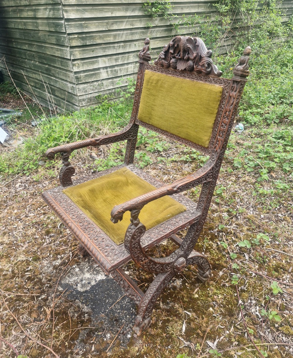 A detailed carved dark wood Anglo-Indian armchair featuring an elephant motif cresting, figural finials, and olive green velvet seat and back upholstery. View II