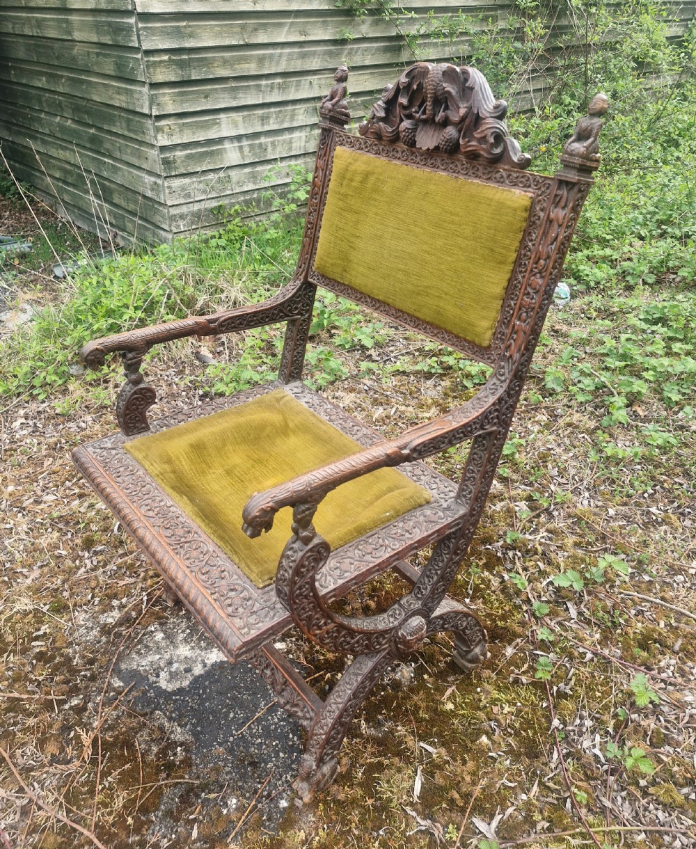 A detailed carved dark wood Anglo-Indian armchair featuring an elephant motif cresting, figural finials, and olive green velvet seat and back upholstery. View III