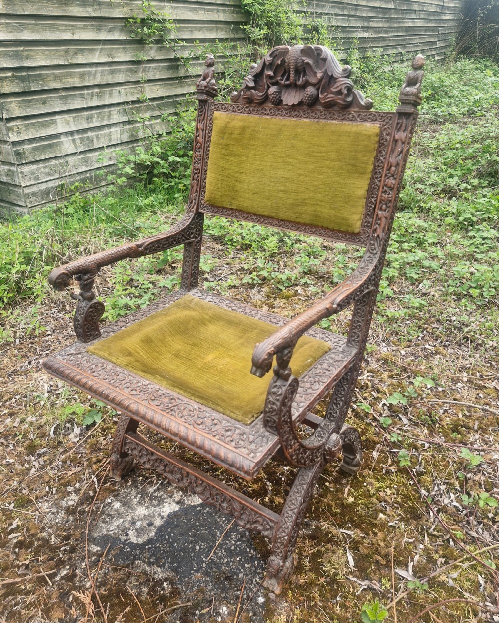 A detailed carved dark wood Anglo-Indian armchair featuring an elephant motif cresting, figural finials, and olive green velvet seat and back upholstery. View V