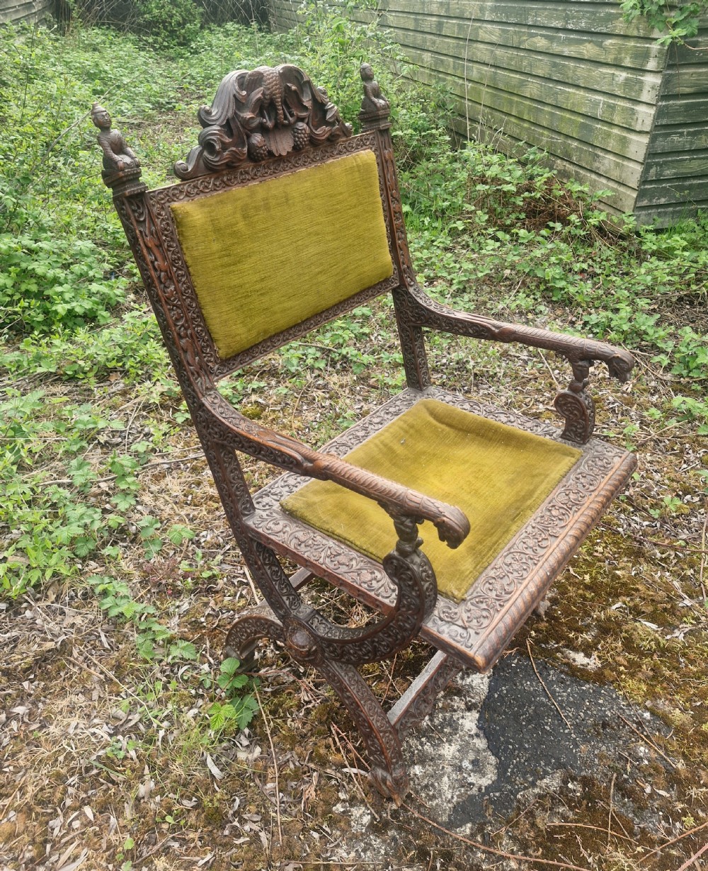 A detailed carved dark wood Anglo-Indian armchair featuring an elephant motif cresting, figural finials, and olive green velvet seat and back upholstery. View VI