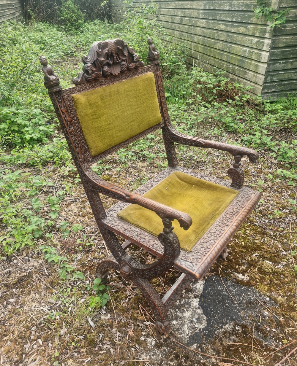 A detailed carved dark wood Anglo-Indian armchair featuring an elephant motif cresting, figural finials, and olive green velvet seat and back upholstery. View VII