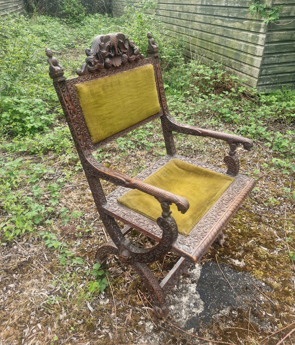 A detailed carved dark wood Anglo-Indian armchair featuring an elephant motif cresting, figural finials, and olive green velvet seat and back upholstery. View VIII