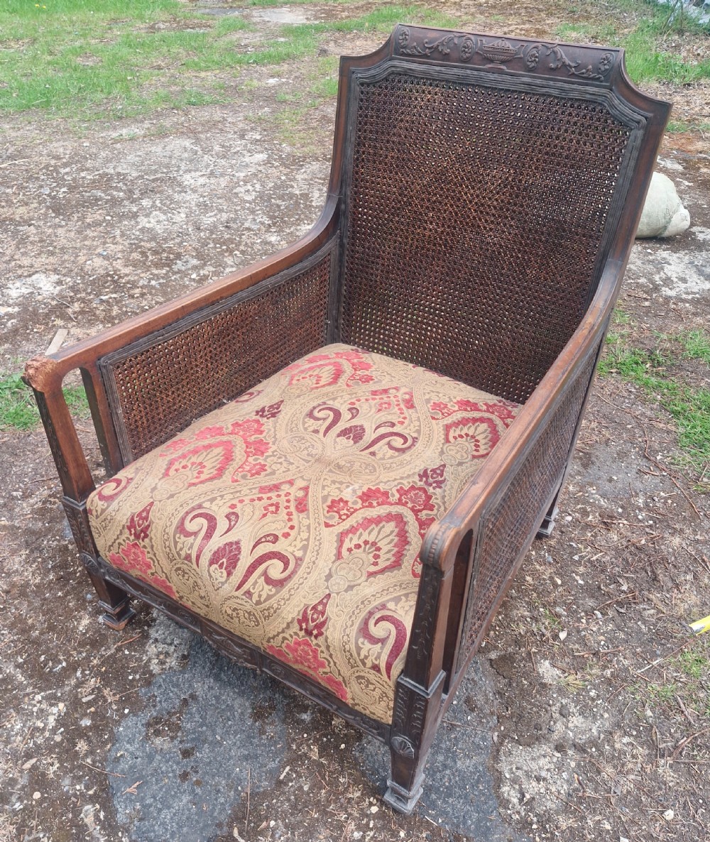 An Edwardian mahogany bergere armchair with woven cane panels on the back and sides and a patterned upholstery seat cushion.