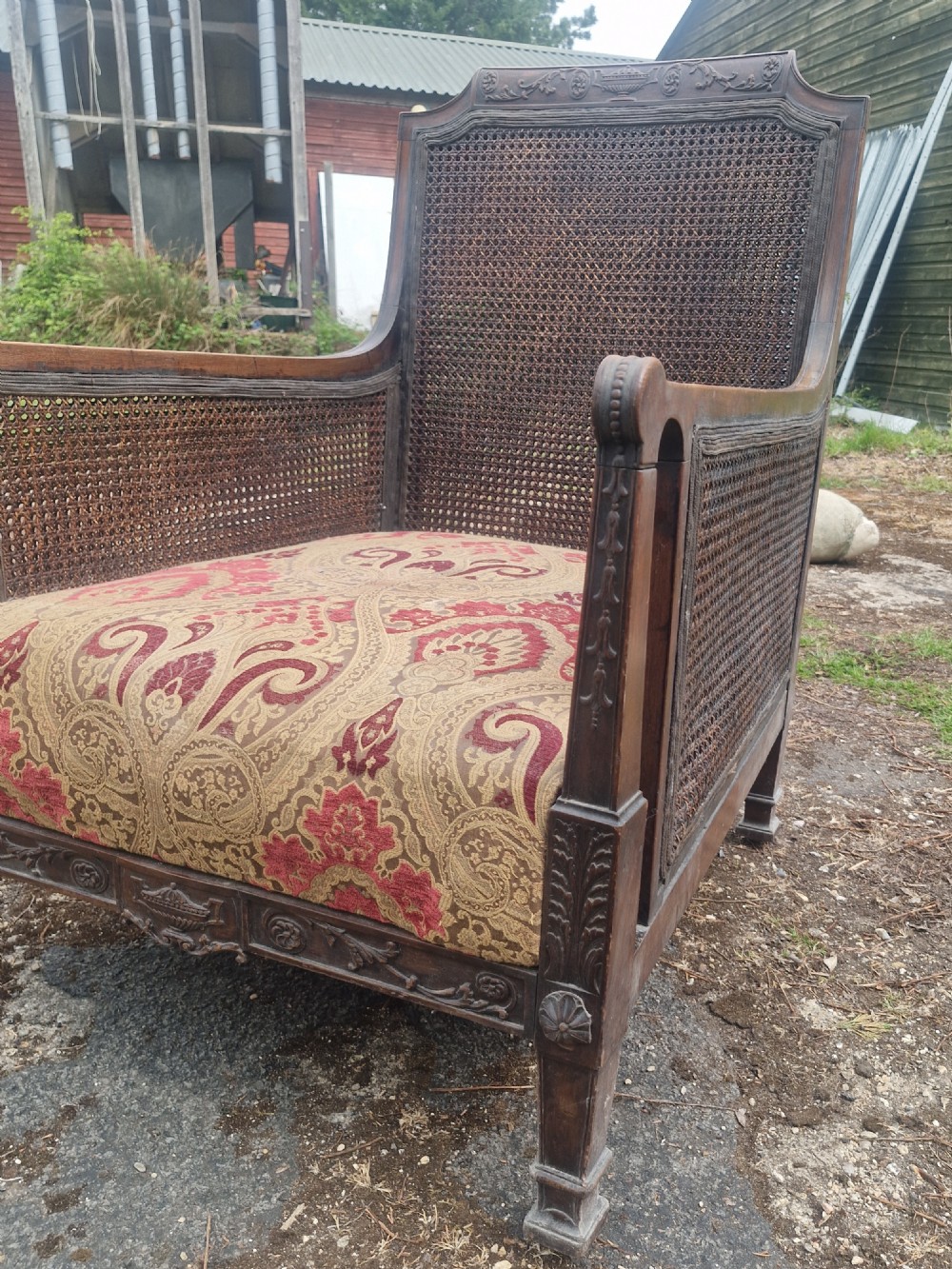 An Edwardian mahogany bergere armchair with woven cane panels on the back and sides and a patterned upholstery seat cushion. View III
