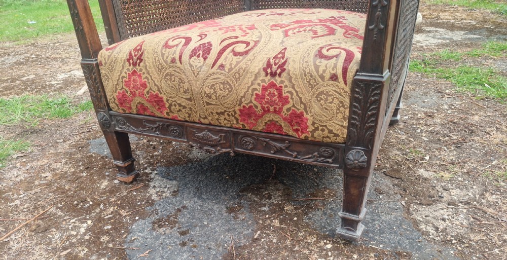 An Edwardian mahogany bergere armchair with woven cane panels on the back and sides and a patterned upholstery seat cushion. View IV